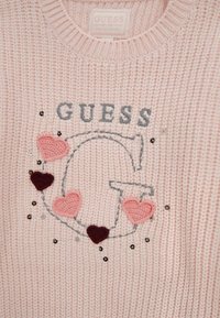 Maglione lavorato a maglia di colore rosa chiaro con una grande "G" ricamata in grigio, circondata da cuori all'uncinetto rosa e marrone scuro, e paillettes sparse.