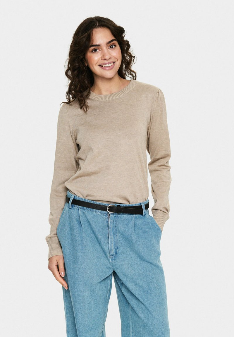 Beige knitted long-sleeve sweater with a round neckline, paired with light blue high-waisted denim trousers and a black belt.