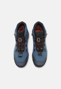 Zapatos de senderismo azules con un upper texturizado, detalles en negro y cordones elásticos naranjas. Cuentan con un forro impermeable Gore-Tex y suelas de goma duraderas.