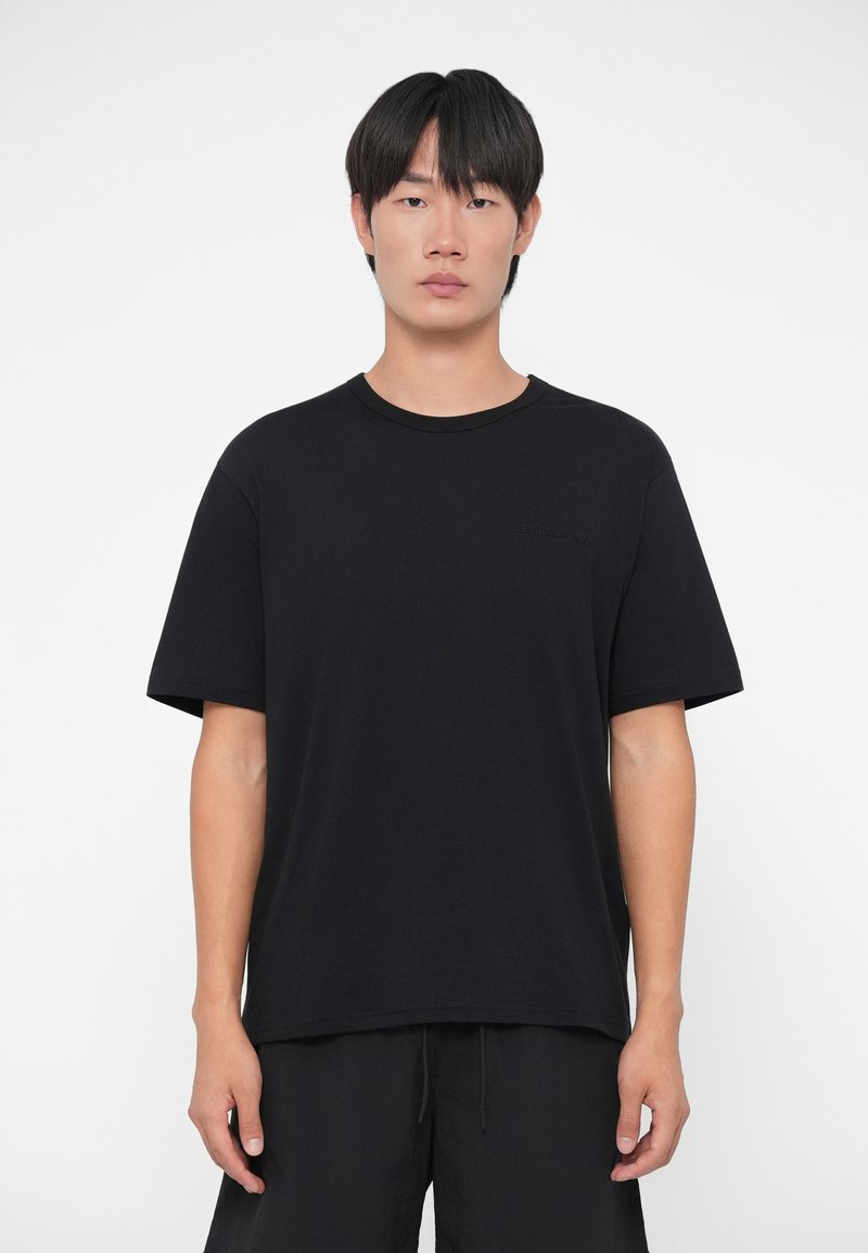 T-shirt nera a maniche corte in cotone, con scollatura rotonda e un logo in rilievo discreto sul petto. Tessuto morbido e vestibilità comoda.
