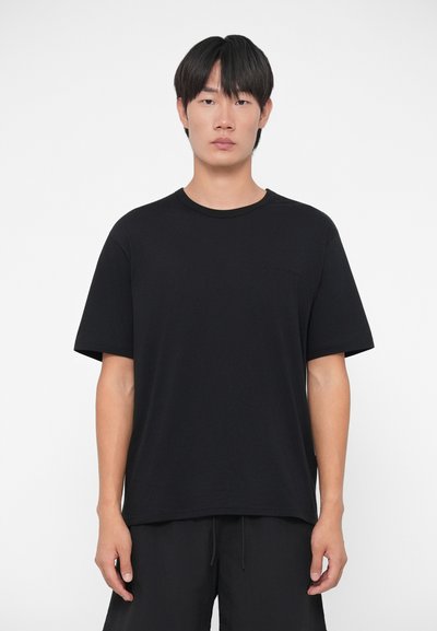 Melna īsām piedurknēm T-kreklu, izgatavotu no kokvilnas, ar apaļu kakla izgriezumu un diskrētu reljefu logotipu uz krūšu daļas. Gluda tekstūra un brīvs piegrieziens.