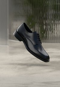 Chaussure habillée en cuir noir à finition lisse, design à lacets, bout arrondi et coutures discrètes, posée sur un fond neutre.