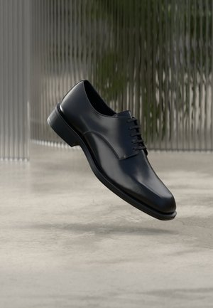 Schwarzer Lederschuh mit glatter Oberfläche, Schnürdesign, abgerundeter Spitze und dezenter Naht, vor neutralem Hintergrund.