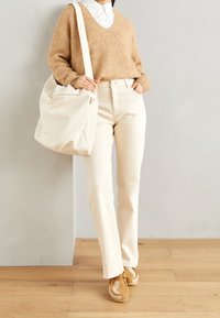 Beige pletený svetr, bílá košilová košile, krémové rovné kalhoty a tan sneakers. Velká plátěná taška na zip.