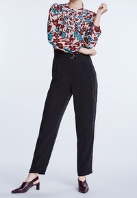 Blouse à motif floral en rose, rouge et bleu, associée à un pantalon noir taille haute. Le mannequin porte des chaussures à talons rouges foncés.