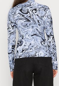 Haut à manches longues avec un motif tourbillonnant noir et bleu clair, texture côtelée, design ajusté, associé à un pantalon noir.