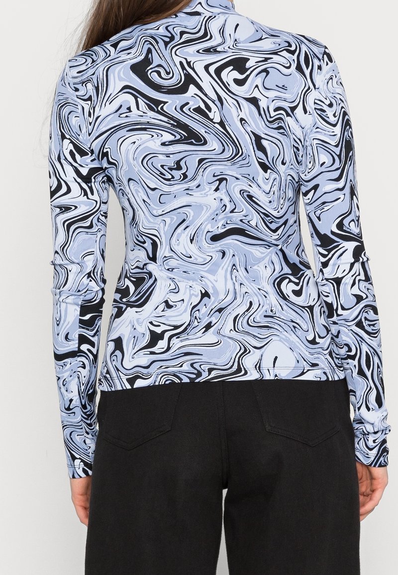 Haut à manches longues avec un motif tourbillonnant noir et bleu clair, texture côtelée, design ajusté, associé à un pantalon noir.