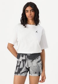 Vit bomull t-shirt med svart Jordan-logga, i kombination med svarta och vita mönstrade shorts med grafiska mönster och texturerade ränder.