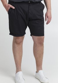 Pantalones cortos de algodón negros con pu�ños doblados, bolsillos laterales y cierre de botón frontal; combinados con zapatillas blancas para un contraste.