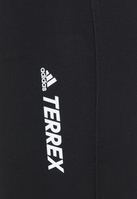 Leggings atléticos negros con una textura suave, con un logo blanco de "adidas" y el texto "TERREX" en el lado izquierdo.