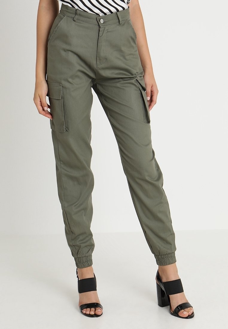 Pantalon cargo vert olive avec poignets élastiques porté avec des sandales noires à talons hauts et un top rayé visible à la taille.
