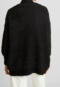 Schwarzer übergroßer Strickpullover mit gerippter Textur und dezenten metallischen Fäden. Verfügt über einen gerundeten Ausschnitt und angesetzte Schultern.