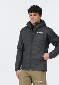 Zwarte gewatteerde jas met een capuchon, voorzien van een ritssluiting en een logo op de borst. Gemaakt van een textuurstof met een quilted ontwerp.
