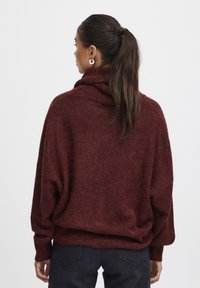 Burgundská oversized mikina s vysokým golierom, pletenou štruktúrou, dlhými rukávmi a voľným strihom. Nosená s tmavými džínsami.