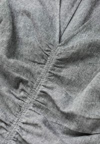 Gros plan sur un tissu gris avec des coutures visibles et une texture froncée, formant de doux plis.