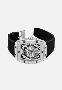 Czarny zegarek na gumowym pasku z metalową prostokątną kopertą. Posiada skomplikowaną szkieletową tarczę, widoczny mechanizm oraz kontrastujące czerwone akcenty.