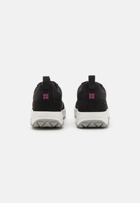 Black athletic shoes with a mesh upper, suede accents, and a white treaded sole. Features pull tabs and a pink logo on the heel.