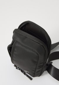 Borsa a tracolla nera in nylon con chiusura a zip, superficie testurizzata, tracolla regolabile e tasca frontale per riporre oggetti.