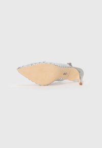 Spissesmussede sølv stilettosko med flettet metallisk overdel og beige såle, hviler på siden mot hvit bakgrunn.