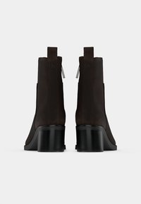 Rjavi usnjeni gležnjarji s sleek dizajnom, zoženimi oblikami in črnimi debelimi petami. Vključujejo zankice za enostavno obuvanje.