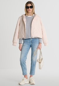 Gaiši rozā quiltota jaka ar kapuci, tumši zils un balts svītrains krekls, zili šauri džinsi, baltas kedas un gaišas krāsas soma.