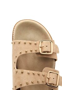 Sandali in suede beige con due cinturini regolabili, finiture dorate e decorazioni con borchie tonde lungo i cinturini. Suola piatta.