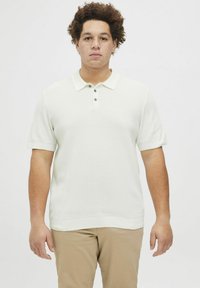 Camisa polo de manga corta color beige claro con tejido texturizado, que presenta un cuello estándar y tres botones verdes en la parte delantera.