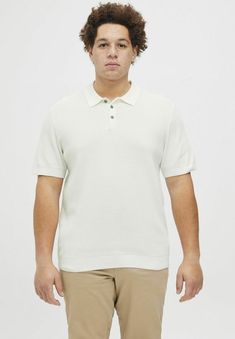 Camisa polo de manga corta color beige claro con tejido texturizado, que presenta un cuello estándar y tres botones verdes en la parte delantera.