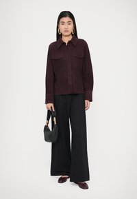 Burgundy button-up shirt with two front pockets, paired with wide black trousers, black handbag, and dark maroon flats. Smooth texture.