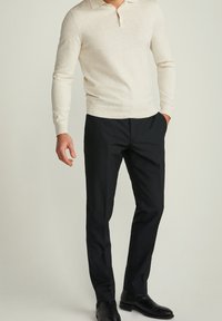 Helles beige langärmeliges Polohemd mit Kragen, kombiniert mit schwarzen Hosen und schwarzen Stiefeletten. Glatte Stofftextur.