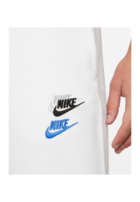 Närbild av vitt tyg med tre broderade Nike-loggor staplade i grått, svart och blått, bredvid en persons hand.