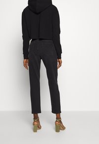 Sudadera negra corta con mangas largas, combinada con pantalones oscuros de color gris, con corte recto y diseño liso. Sandalias de tacón bloque verde.