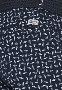 Marinfärgade tygshorts med ett vitt pillerformat mönster. Inkluderar en etikett på bakfickan med varumärkesinformation.