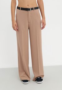 Pantalones de pierna ancha en tela de color beige claro, que presentan un cinturón negro con una hebilla de metal. Textura suave, diseño ajustado y pliegues frontales visibles.