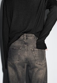 Maglietta nera a maniche lunghe abbinata a jeans a gamba larga grigi sbiaditi. Caratteristiche notevoli includono tasche strutturate e un design classico della vita.
