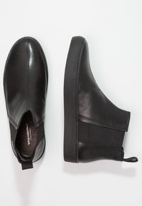 Botas de tobillo de cuero negro con un acabado suave, paneles laterales elásticos, punta redonda y suelas de goma, con tiradores para facilitar el acceso.