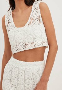 Frau trägt weißes Häkel-Crop-Top und passenden hochgeschnittenen Rock mit kunstvollen floralen Spitzenmustern.