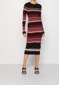 Robe en maille avec manches longues, encolure ronde et silhouette ajustée. Rayures verticales aux motifs noirs, rouges, roses et blancs.