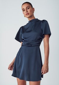 Navy blue satin mekko, jossa on korkea kaula-aukko, lyhyet puffihihat ja sovitettu vyötärö, joka levenee hieman helman kohdalla. Sileä pinta.