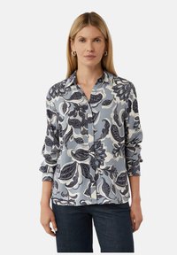 Bluse mit blauem Blumenmuster, Kragen, Knopfleiste und langen Ärmeln. Gefertigt aus einem glatten, weichen Stoff und mit filigranen Blattmustern.