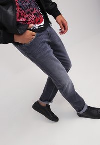 Jeans gris de corte ajustado con una textura desgastada, dobladillos enrollados y bolsillos frontales, combinados con una chaqueta de cuero negra y zapatillas negras.