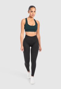 Mustat korkeavyötäröiset trikoot yhdistettynä tummanvihreään urheiluliivimekkoon; molemmat joustavaa kangasta, sopivat urheilutoimintaan.