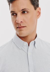 Pasiasta koszula z guzikami w kolorze białym i niebieskim, wykonana z bawełny, z wąskim kołnierzykiem i guzikami z przodu. Posiada subtelną teksturę i prosty krój.