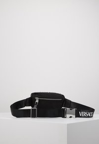 Borsa in nylon nera a vita con zip argentata, tracolla regolabile e un logo bianco audace sulla tracolla. Presenta una texture liscia e un design minimalista.