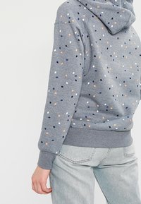 Felpa grigia realizzata in tessuto morbido, con un motivo sparso di piccoli rombi blu, arancioni e bianchi, dotata di cappuccio con cordino e polsini a costine.