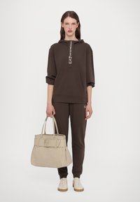 Brown hooded sweatshirt and joggers with logo accents, paired with a textured beige handbag. Footwear is light-colored with a gum sole.
