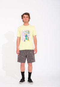 Camiseta gráfica de color amarillo claro con un diseño multicolor en la parte frontal, combinada con pantalones cortos de patrón en blanco y negro.