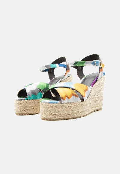 Sandales compensées colorées à motifs géométriques avec brides à la cheville et talons compensés recouverts de jute sur fond blanc.