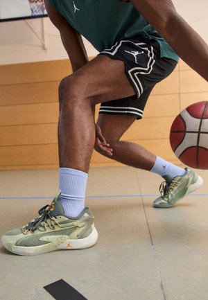 Personne portant des chaussures de basketball dribble un ballon sur un terrain intérieur près d'un panier.