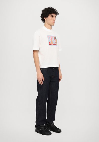 Witte katoenen t-shirt met een kleurrijk grafisch ontwerp aan de voorkant, gecombineerd met donkere spijkerbroek en zwarte sneakers. Rechte pasvorm, korte mouwen.